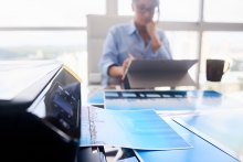 Woman working in an office and close-up of printer printing picture on paper