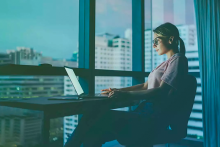 Woman working on laptop at desk against condo windows