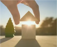 hand putting a wooden roof on play wooden house with sun shining through